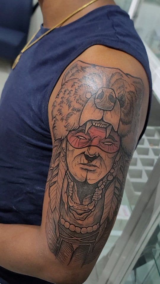 Black and grey Chief beneath a bear headdress tattoo on the upper arm, by Soulraven Studios in Kingston, Jamaica