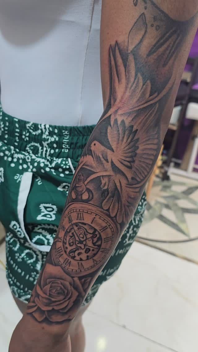 Black and grey Bird, pocket watch and rose tattoo on the forearm, by Soulraven Studios in Kingston, Jamaica