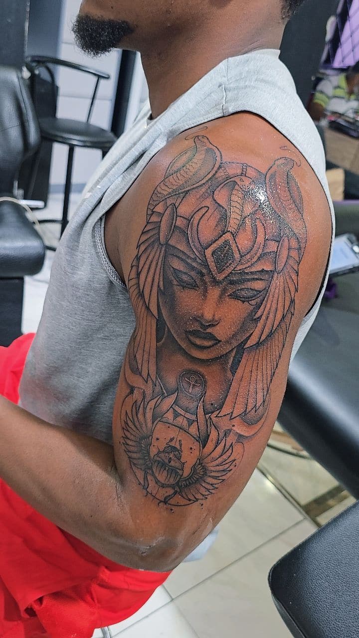 Black and grey Egyptian queen with cobra headdress tattoo on the upper arm, by Soulraven Studios in Kingston, Jamaica