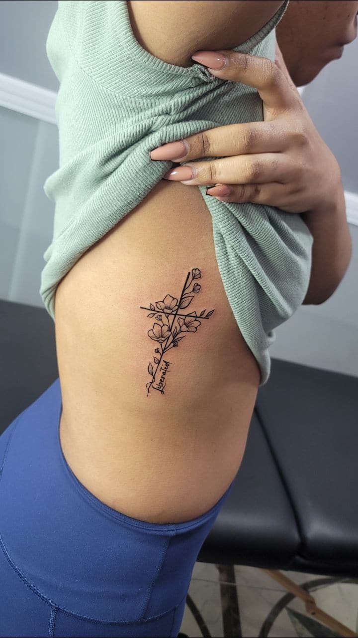 Black and grey Floral cross with a name tattoo on the ribs, by Soulraven Studios in Kingston, Jamaica