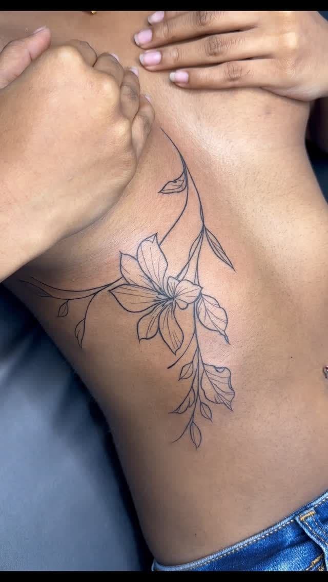 Black and grey Fine-line lily tattoo on the ribs, by Soulraven Studios in Kingston, Jamaica