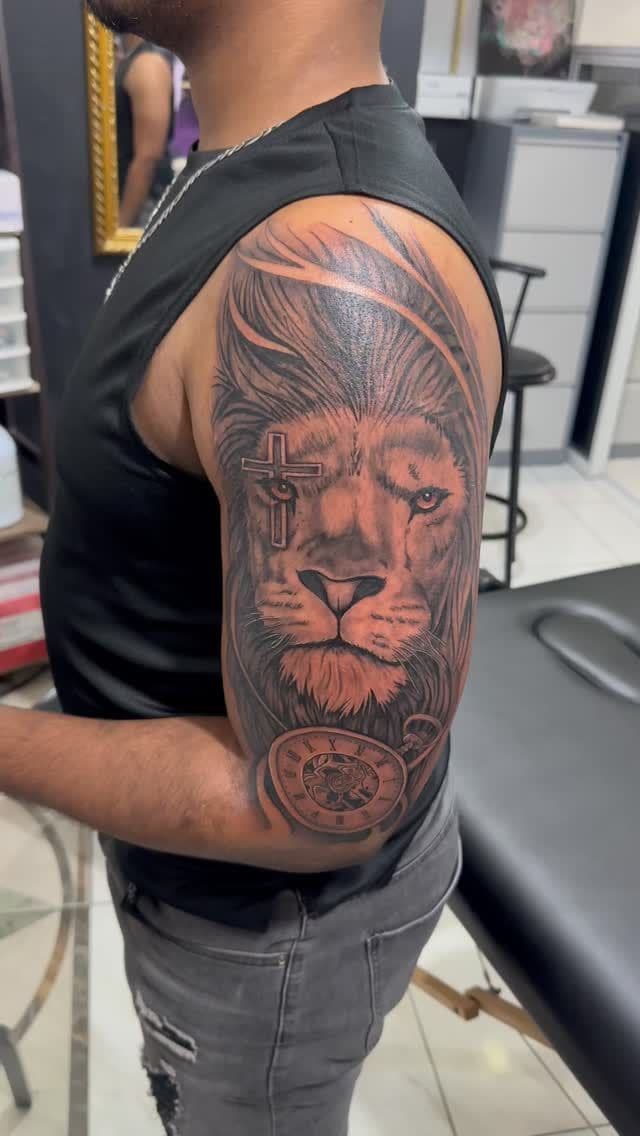 Black and grey Lion with a cross tattoo on the upper arm, by Soulraven Studios in Kingston, Jamaica