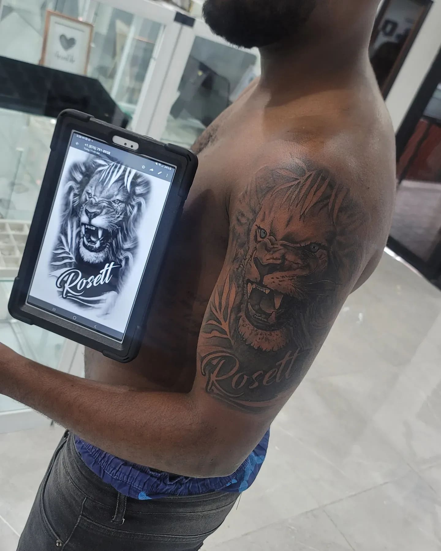 Black and grey Roaring lion with a name in script tattoo on the upper arm, by Soulraven Studios in Kingston, Jamaica