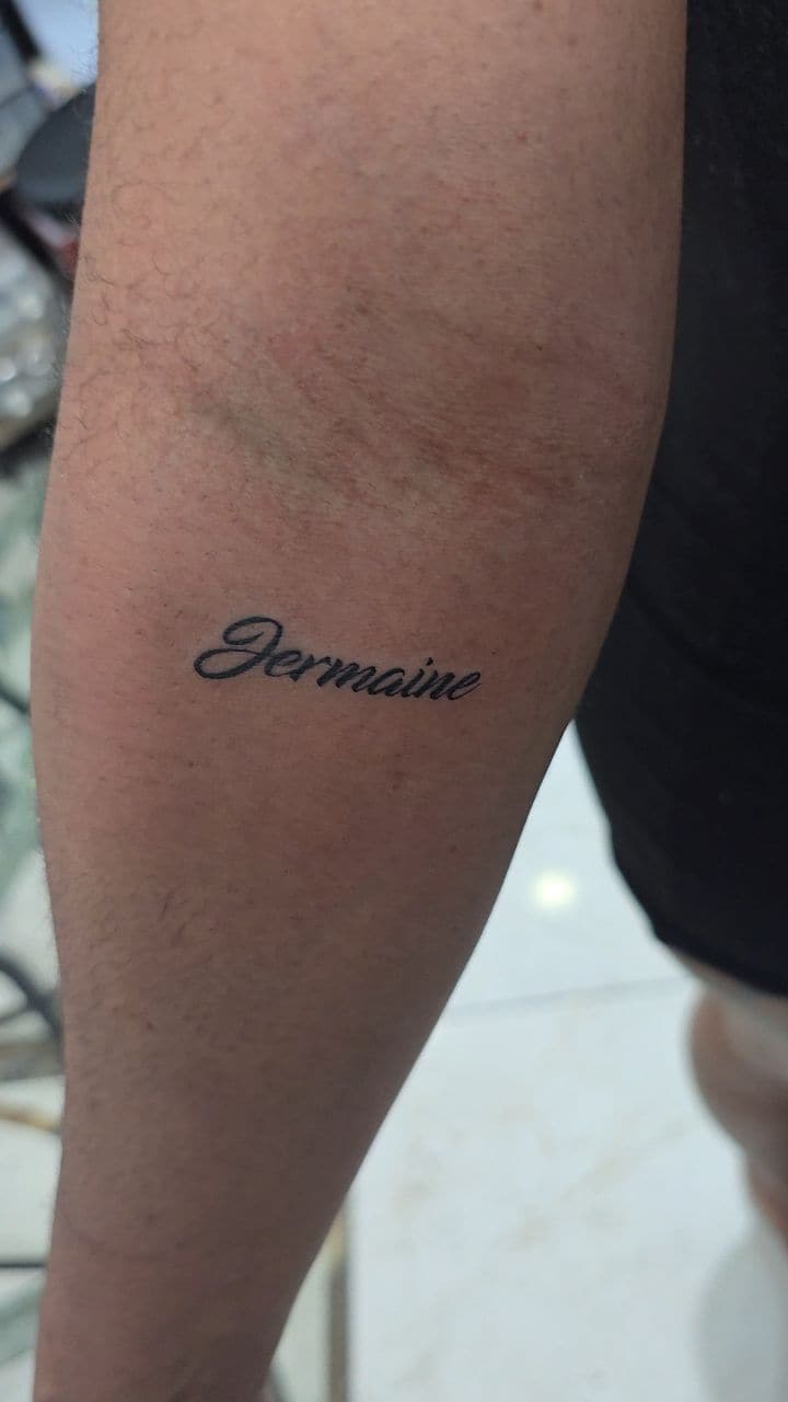 Black and grey Name in cursive script tattoo on the upper arm, by Soulraven Studios in Kingston, Jamaica