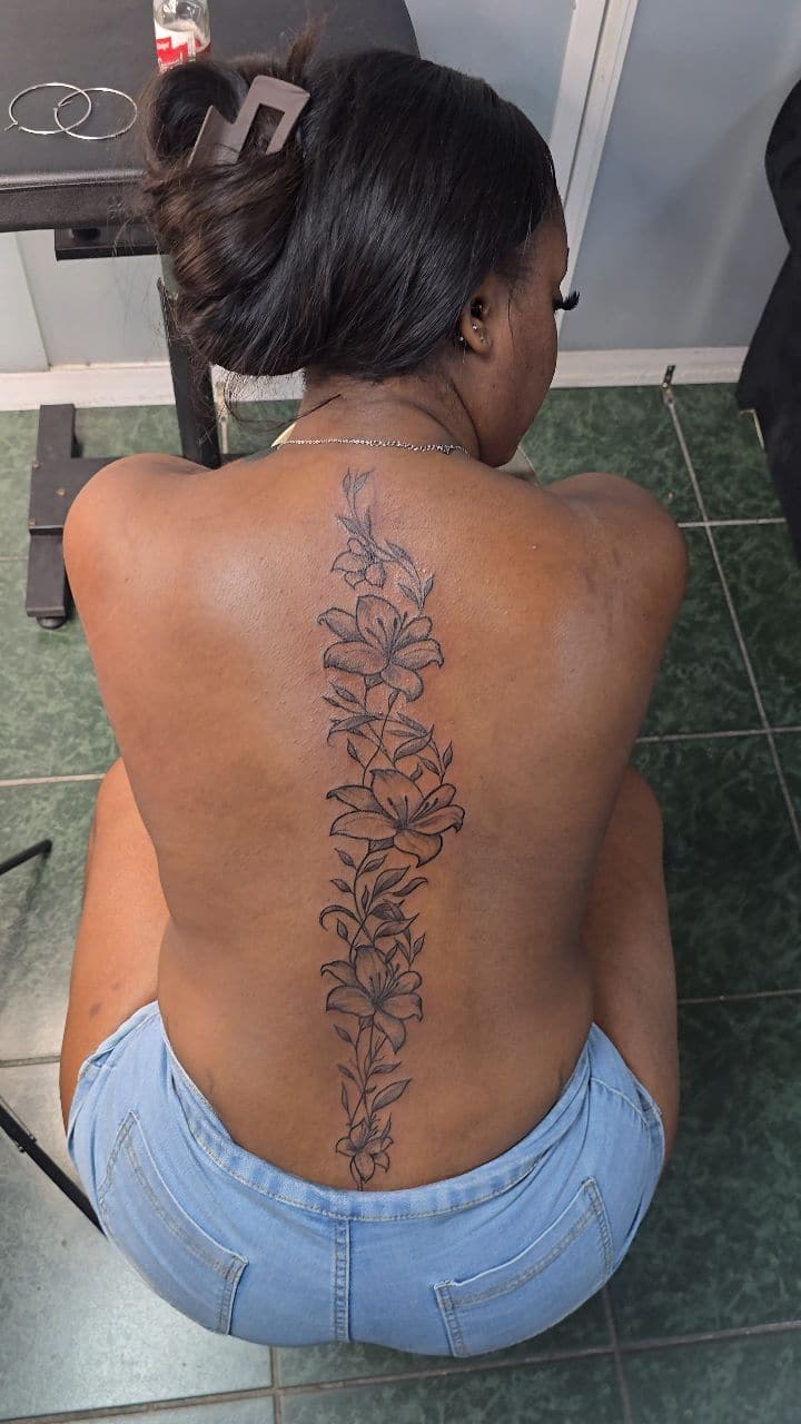 Black and grey Fine-line lilies tattoo on the spine, by Soulraven Studios in Kingston, Jamaica