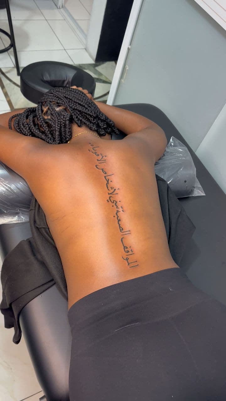 Black and grey Arabic script tattoo on the spine, by Soulraven Studios in Kingston, Jamaica